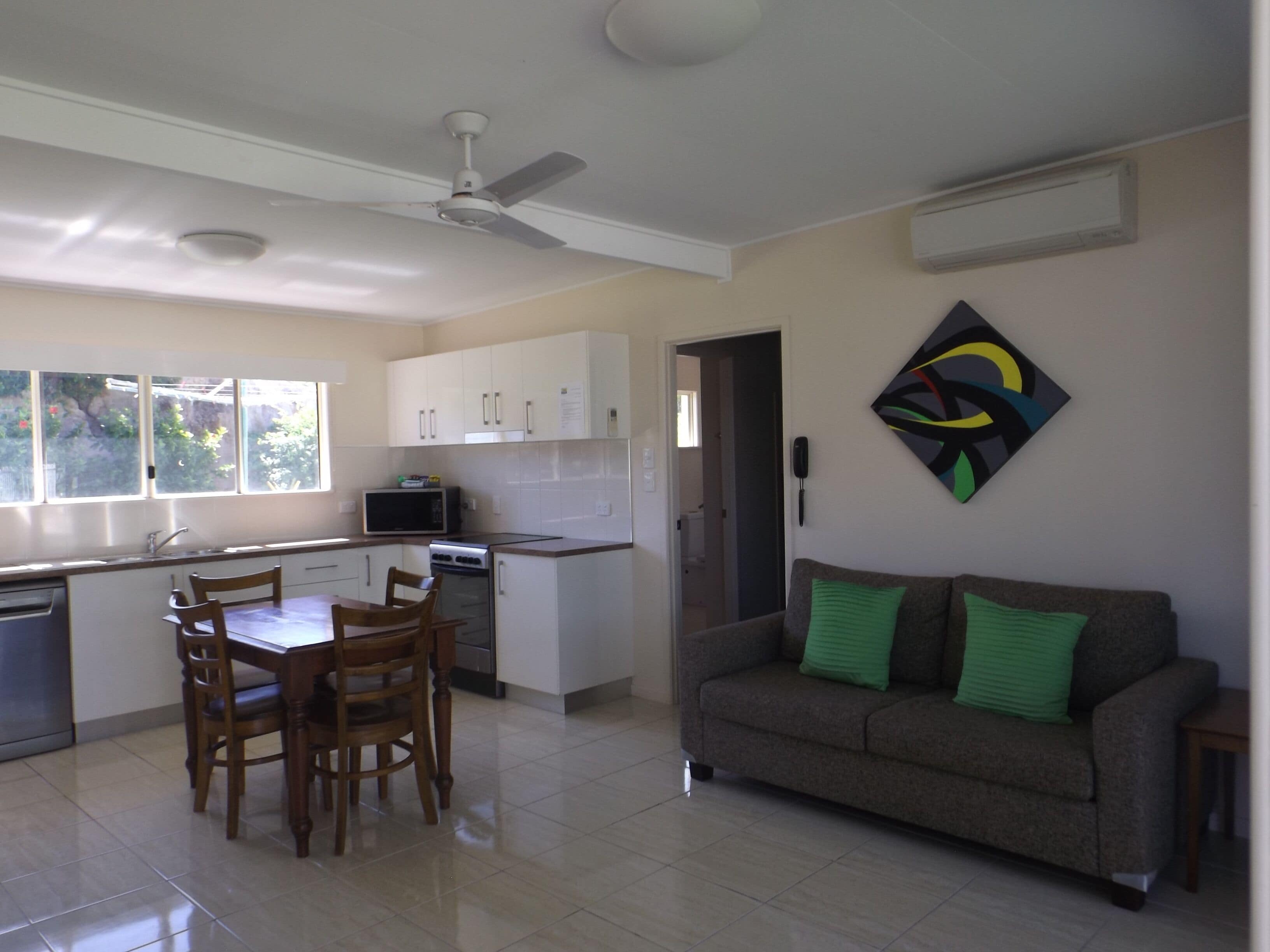 A modern kitchen with white cabinets, a dining table with chairs, a microwave, and a ceiling fan.