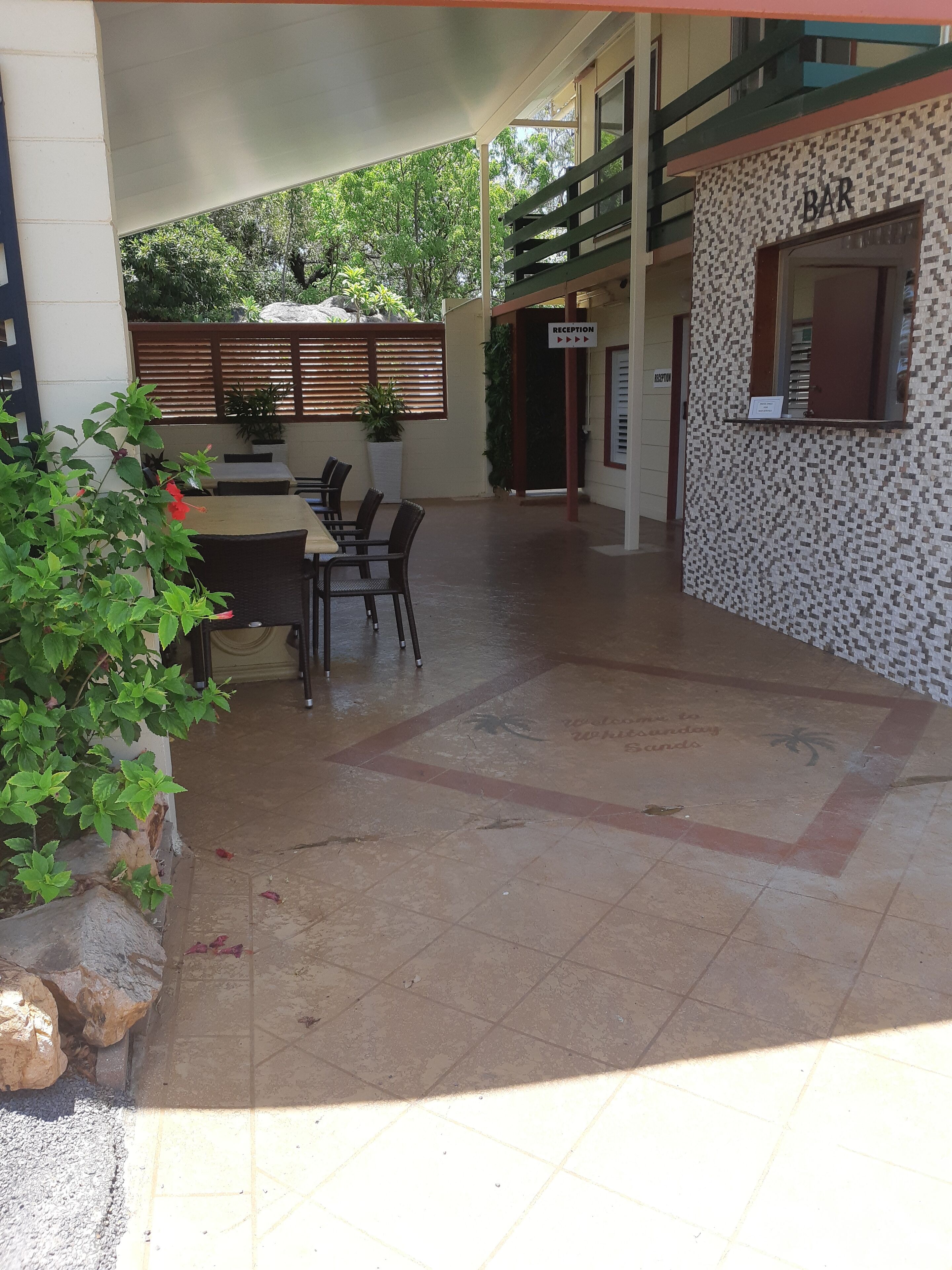An outdoor seating area with tables and chairs, a reception desk, and a building with a patterned facade.