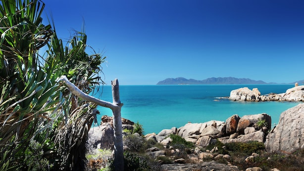 A coastal landscape with rocky terrain, a clear blue sky, and a distant view of mountains. - Whitsunday Sands Resort (Bowen)