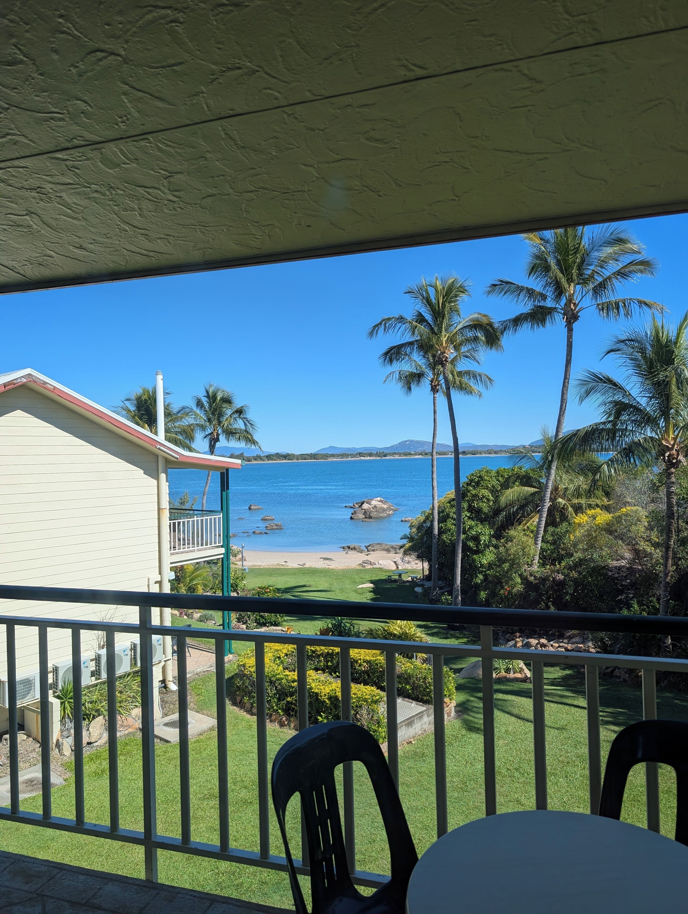 A balcony with a view of a beach, palm trees, and a clear blue sky.