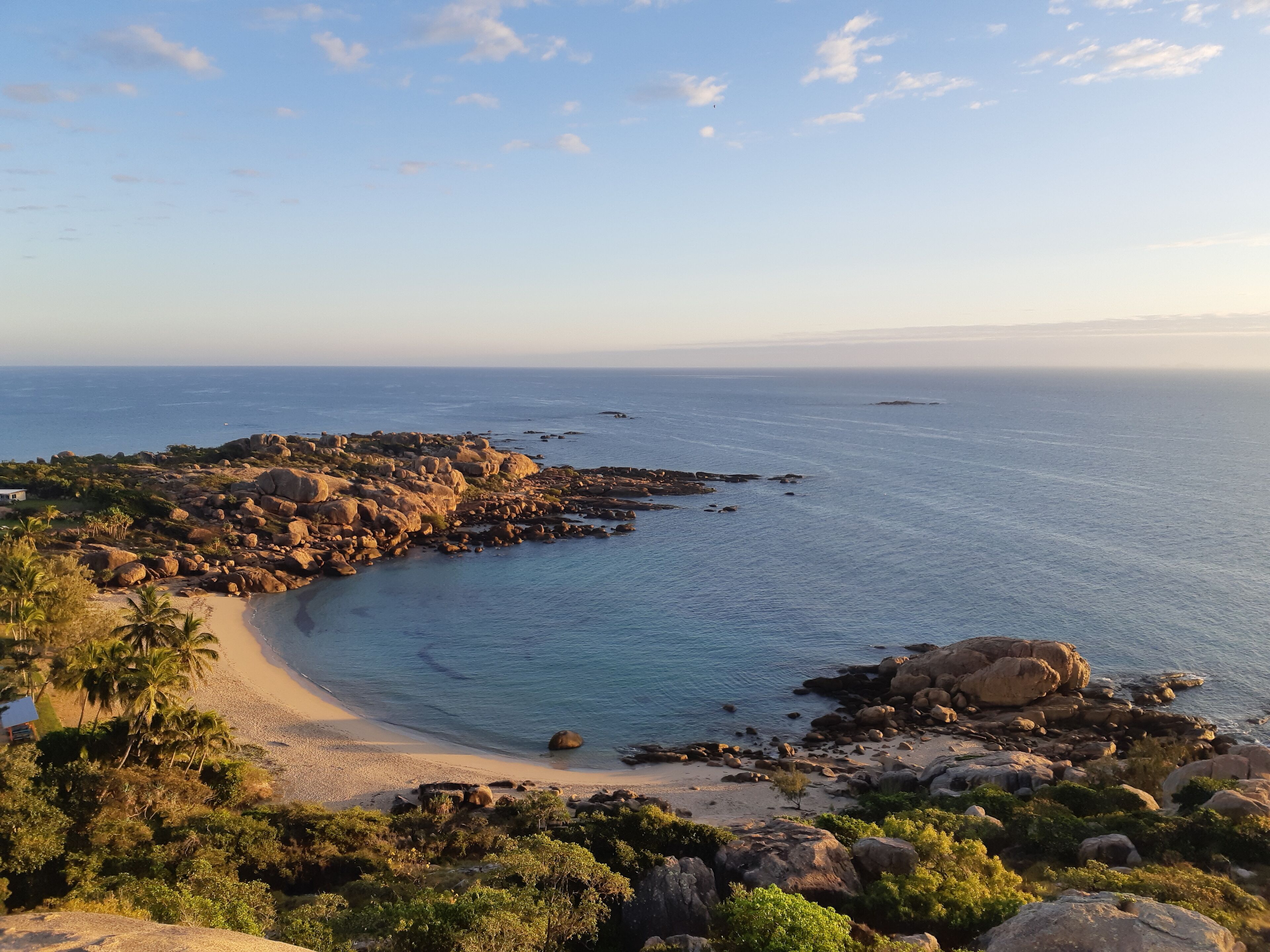Un paisaje costero con una playa arenosa, afloramientos rocosos y abundante vegetación.
