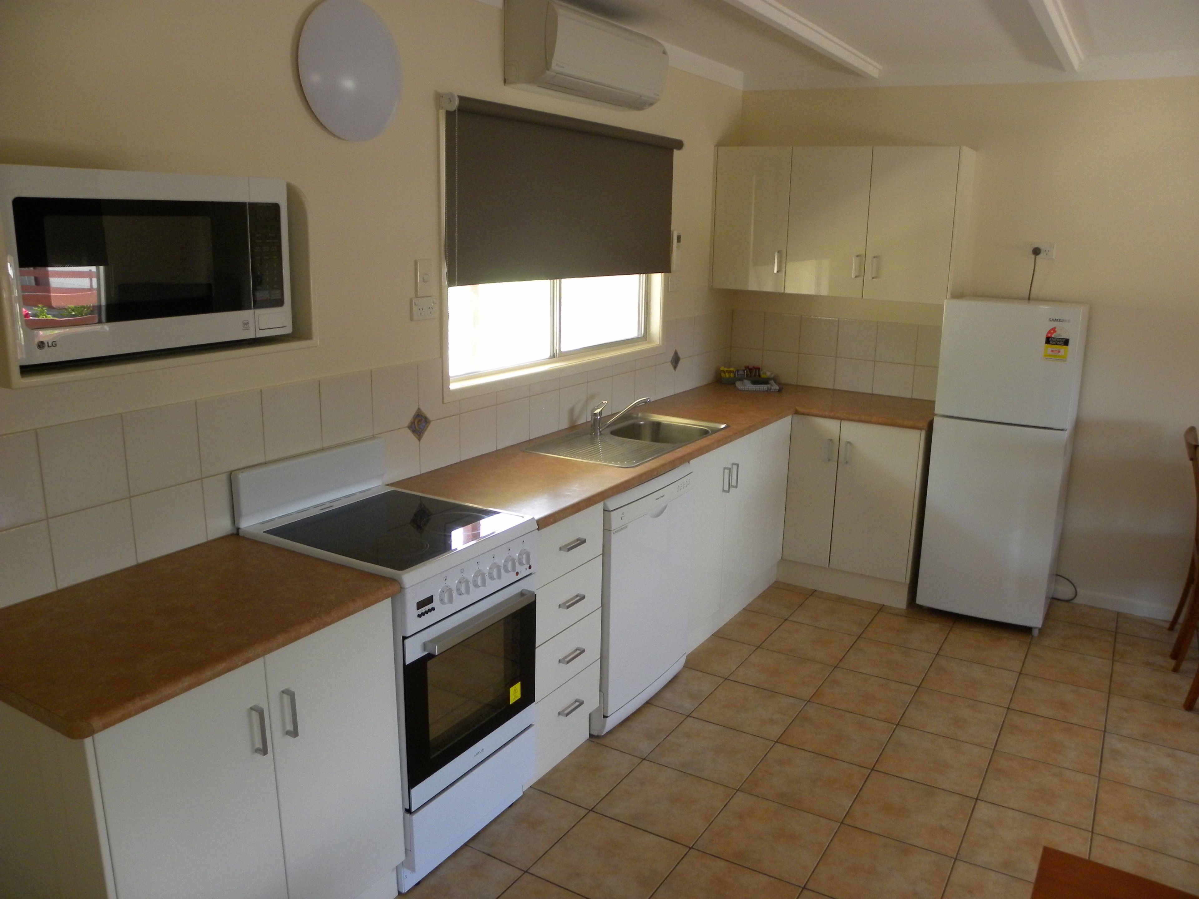 A kitchen with white cabinets, a microwave, a stove, a sink, and a refrigerator.