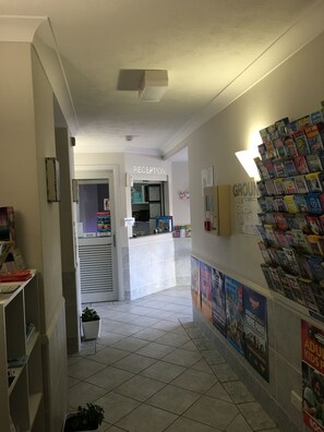 Aula, jossa on vastaanottotiski, ilmoitustaulu ja seinä, jossa on lehtiä.
