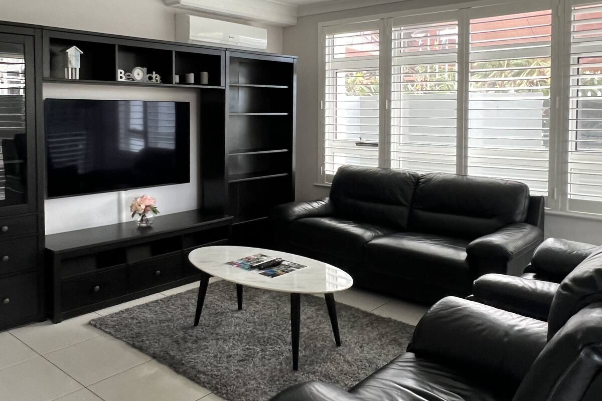Un salon moderne avec un canapé en cuir noir, une table basse blanche et un téléviseur à écran plat posé sur un meuble multimédia noir.