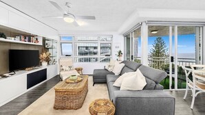 A modern living room with a grey sofa, a flat-screen TV, and a balcony with a view of the city. - Wharf Boutique Apartments (Surfers Paradise)