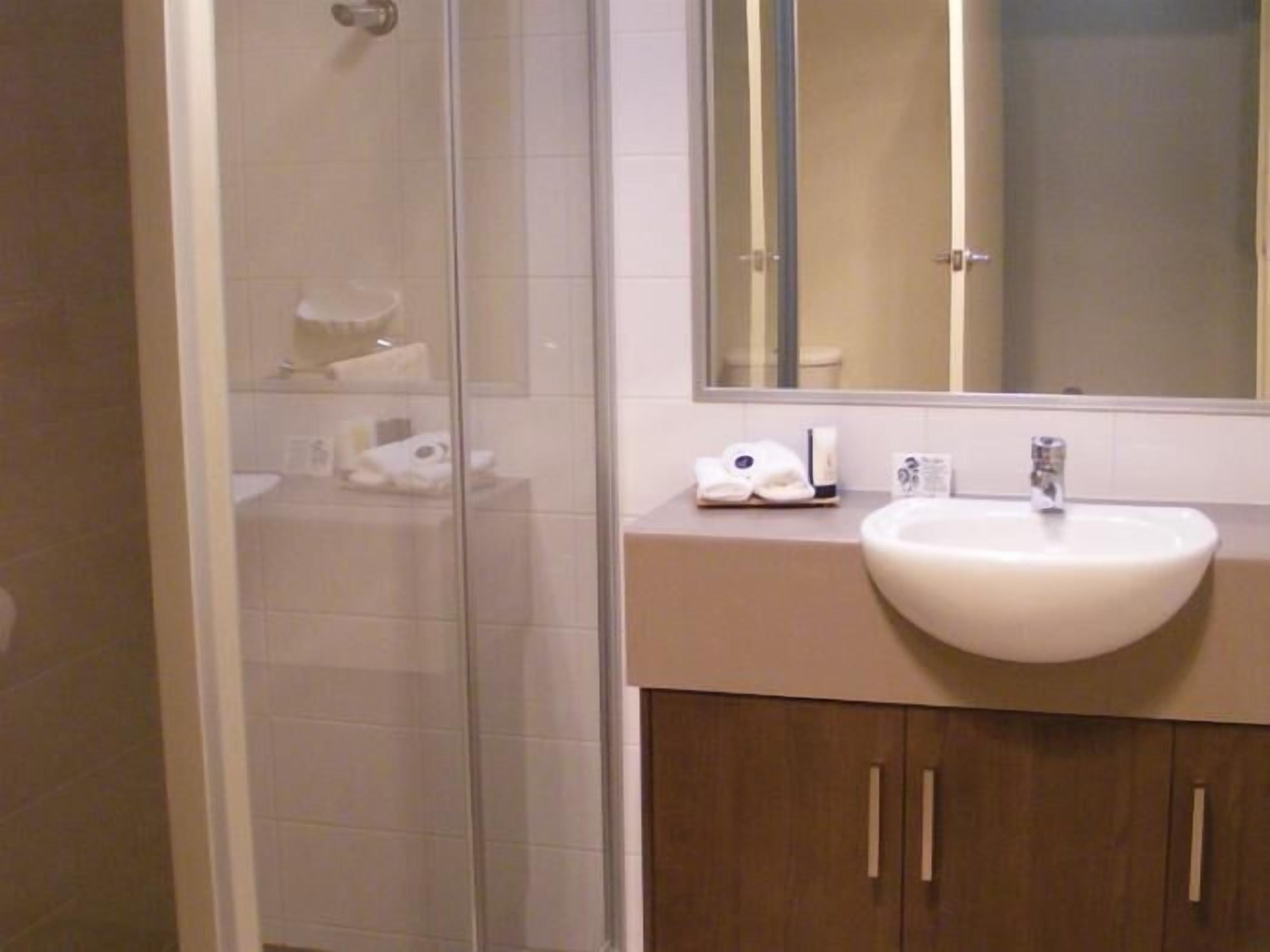 Ein Badezimmer mit Duschkabine aus Glas, einem weißen Waschbecken und einem Spiegel darüber.