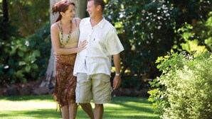 A couple standing in a lush garden with dense foliage and a tree trunk in the background. - Rich River Golf Club Resort (Moama)