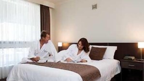 A hotel room with a large bed, a bedside table, and a window with curtains. - Rich River Golf Club Resort (Moama)