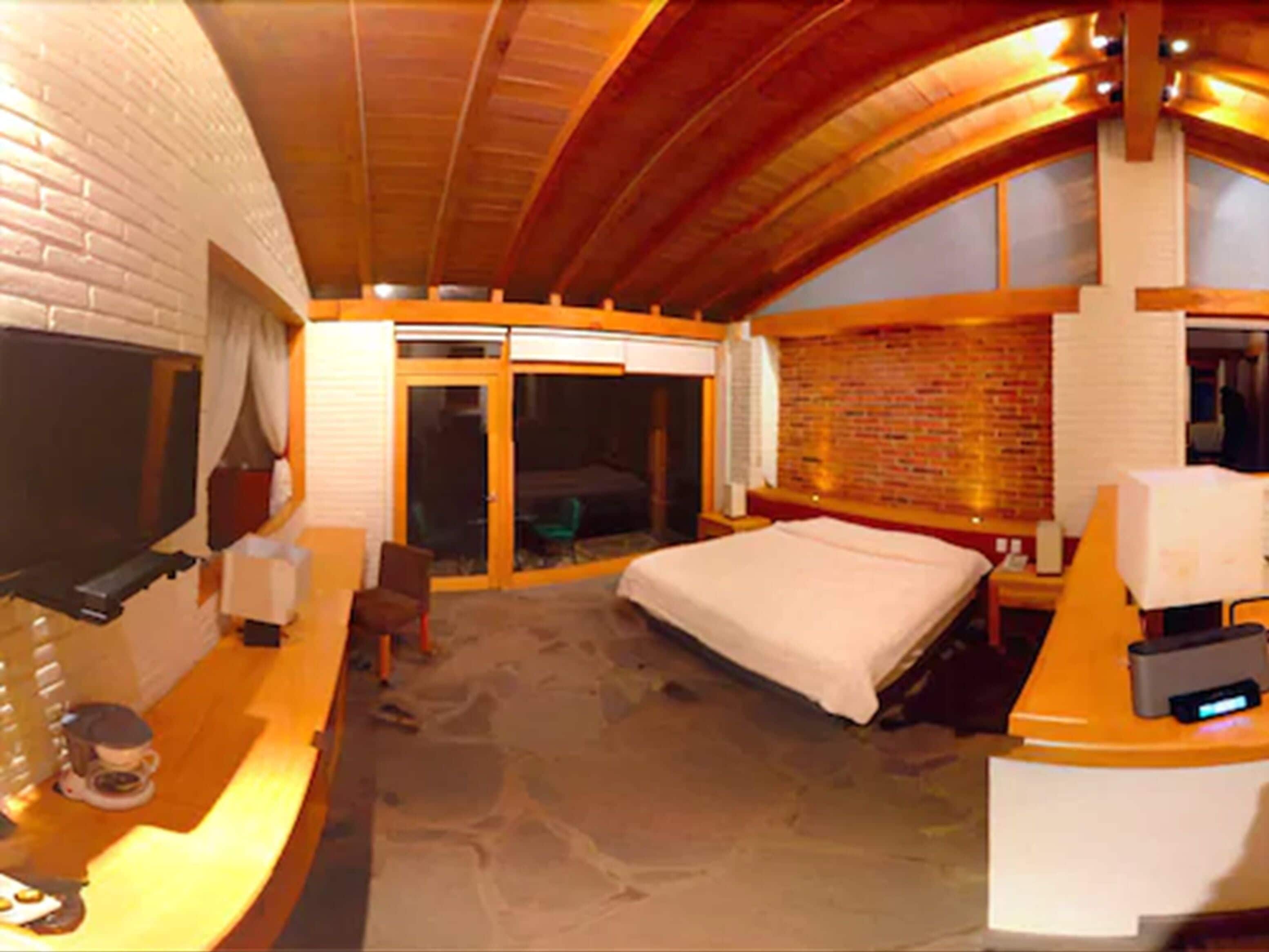 A hotel room with a bed, a desk, a chair, a TV, and a sliding door to the balcony.
