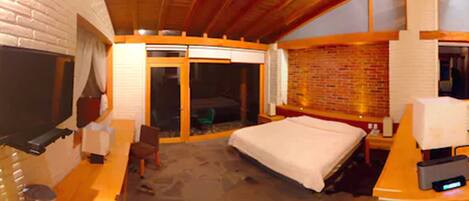 A hotel room with a bed, a desk, a chair, a TV, and a sliding door to the balcony.