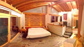 Un dormitorio espacioso con suelo de piedra, una cama grande, techo de madera y pared de ladrillo.