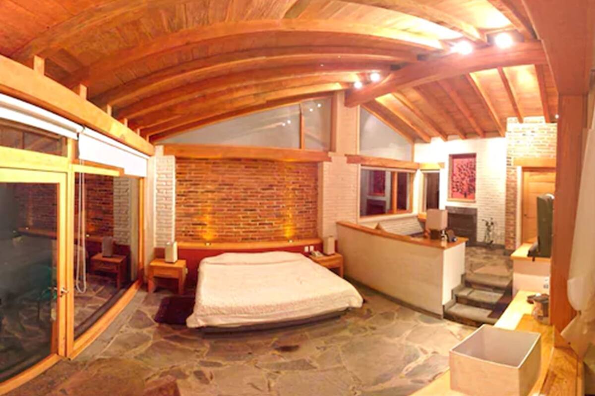 A spacious bedroom with a stone floor, a large bed, a wooden ceiling, and a brick wall.