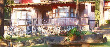 A rustic cabin with a stone foundation, a red roof, and a balcony.