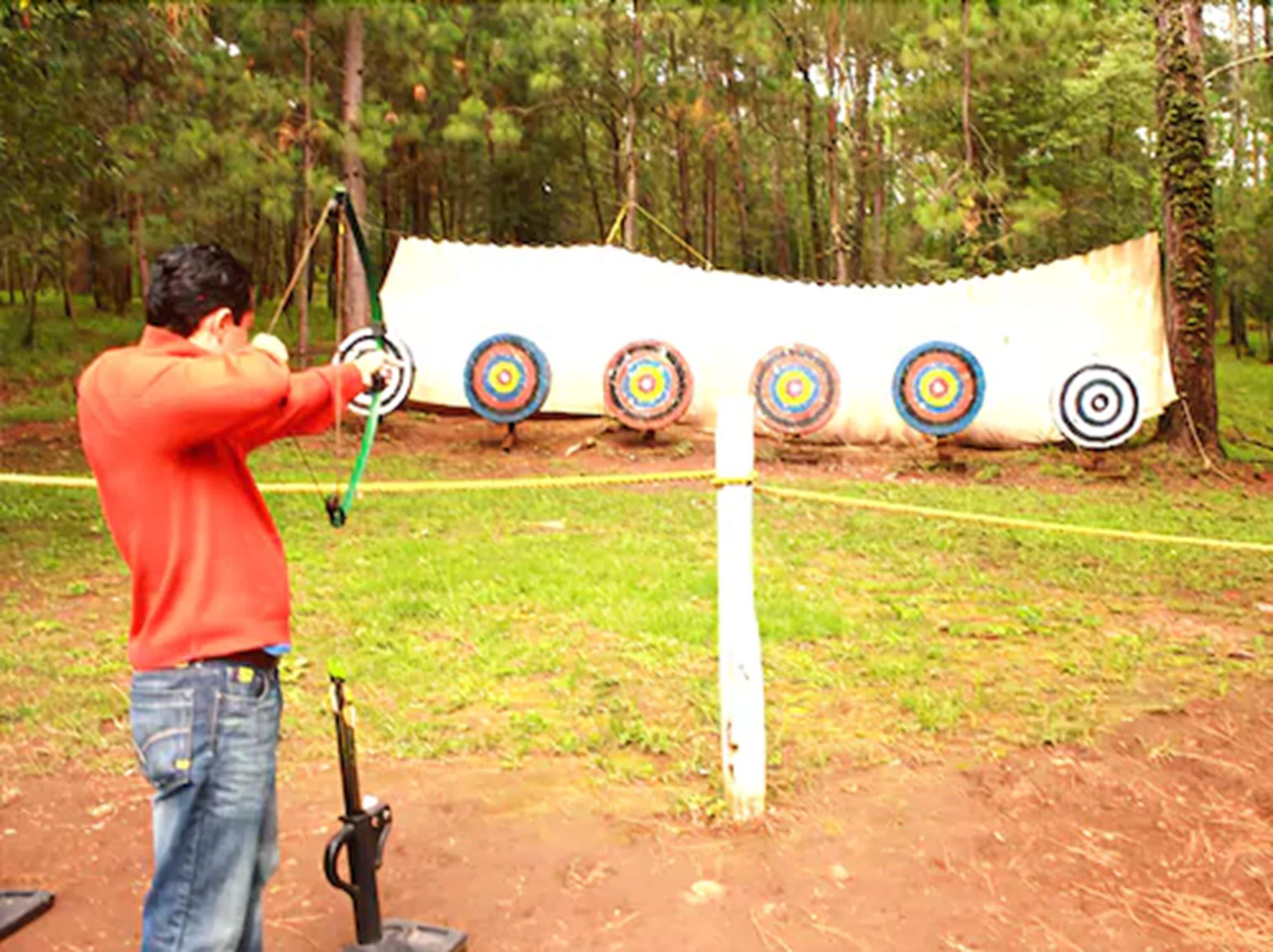 A person aiming a bow at a target with five circular bullseyes.