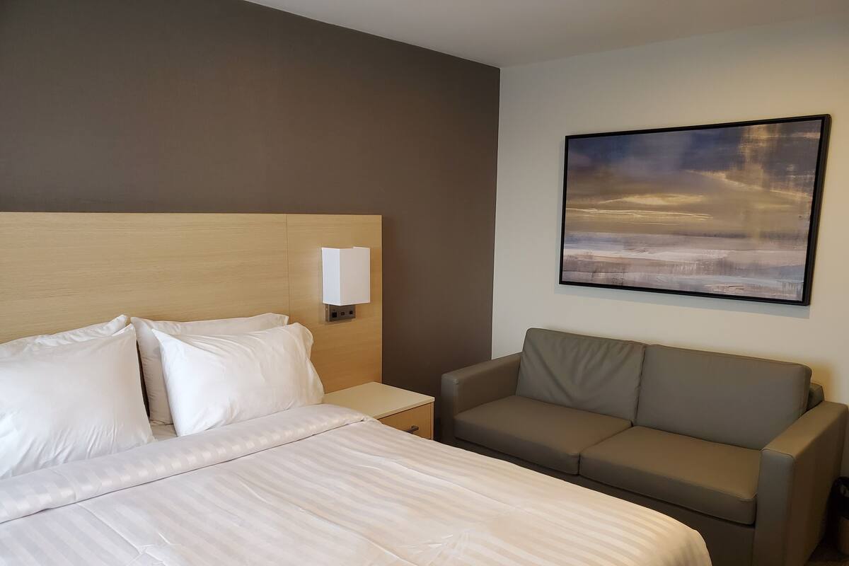 A hotel room with a large bed, a sofa, a nightstand, and a wall-mounted lamp.