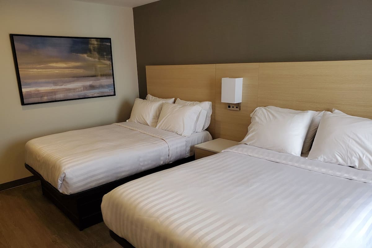 A hotel room with two single beds, a nightstand, a wall-mounted lamp, and a painting on the wall.