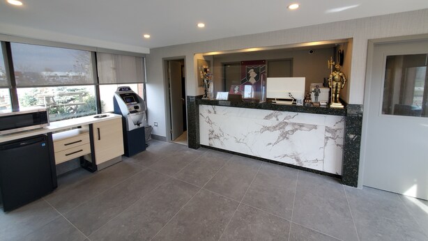 A modern hotel lobby with a marble reception desk, an ATM, and a view of the city through large windows. - White Knight Motel (Mississauga)