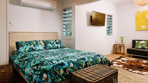 A bedroom with a bed, a wicker chair, a cowhide rug, a small table, and a wall-mounted TV. - The Little Bush Hut (Nelly Bay)