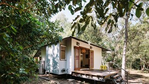 A small, single-story house with a wooden deck and a staircase leading to a door. - The Little Bush Hut (Nelly Bay)