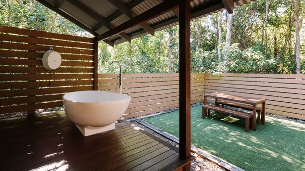 A wooden deck with a large bathtub, a wooden bench, and a wooden fence. - The Little Bush Hut (Nelly Bay)