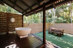 A wooden deck with a large bathtub, a wooden bench, and a wooden fence. - The Little Bush Hut (Nelly Bay)