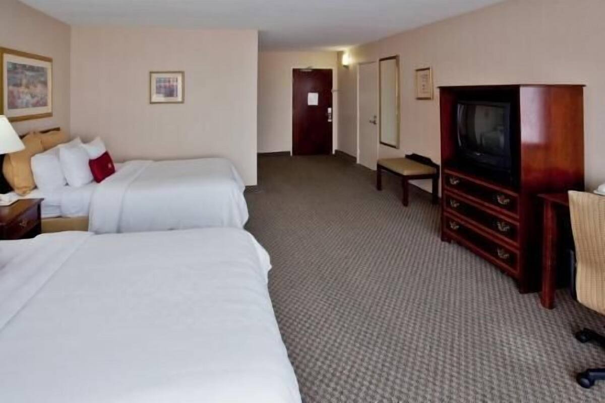 Une chambre d’hôtel avec deux lits, une télévision, un bureau avec une lampe et une chaise.