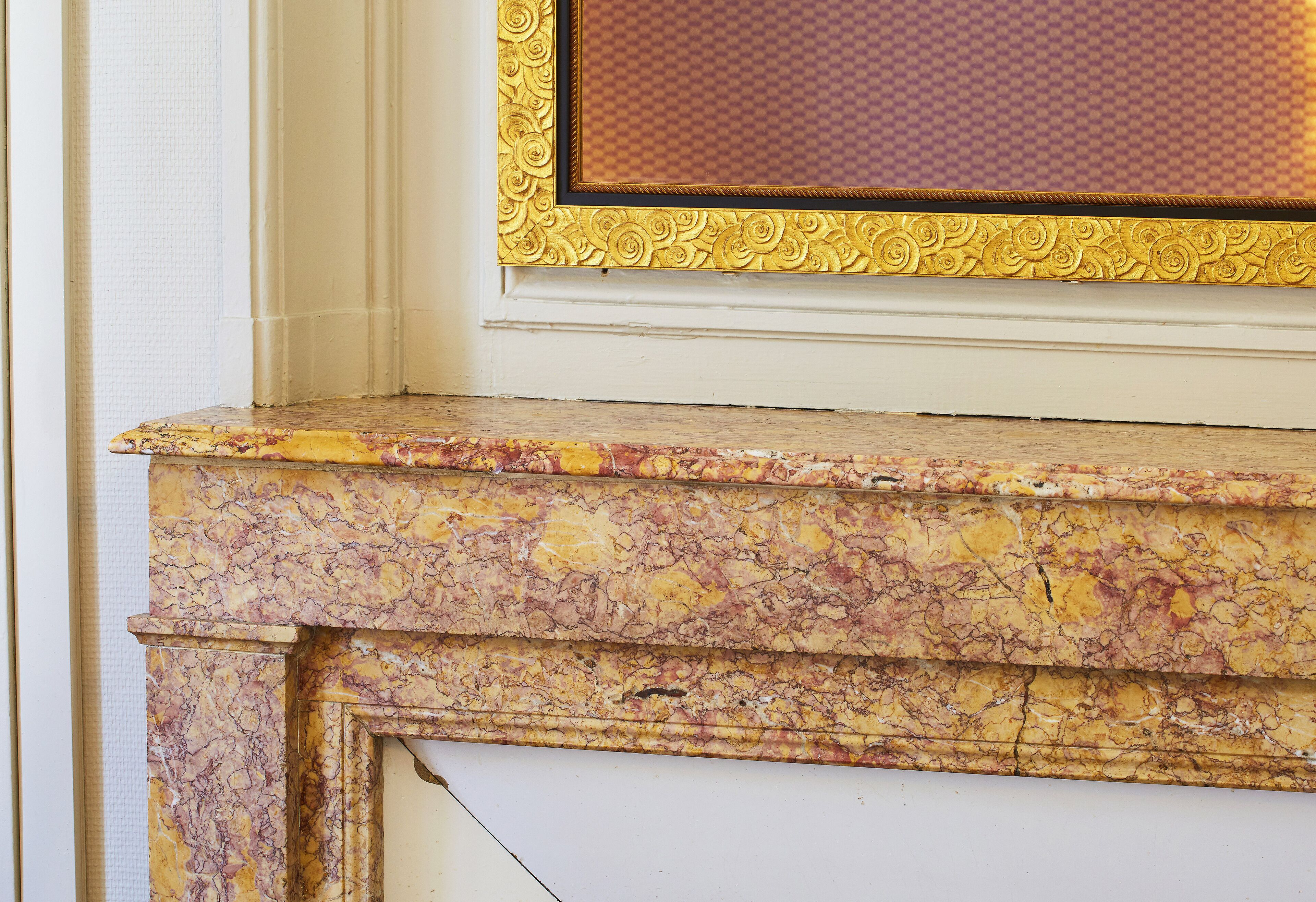 A marble fireplace with a gold ornate frame.