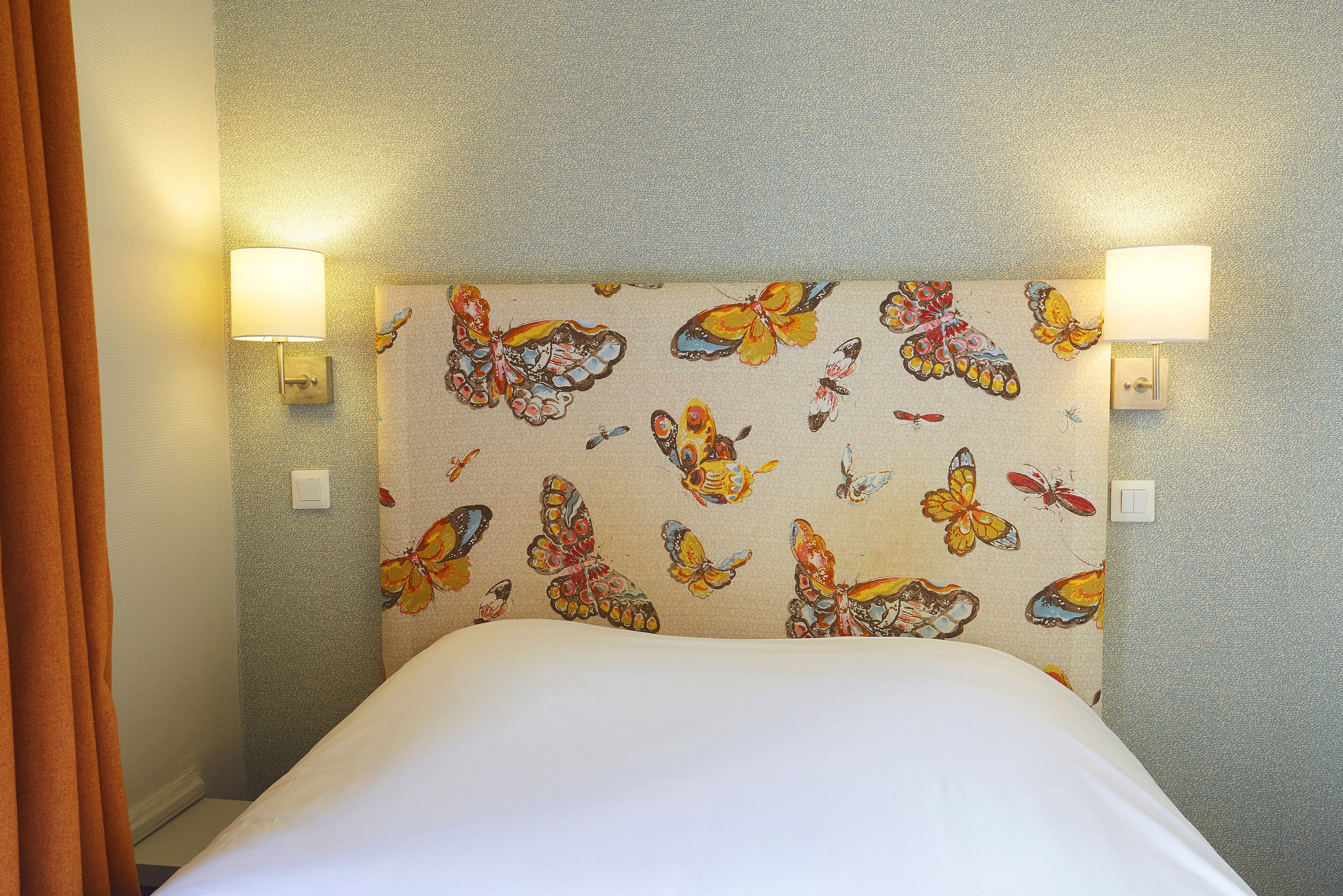 A hotel room with a bed, two wall-mounted lamps, and a butterfly-patterned headboard.