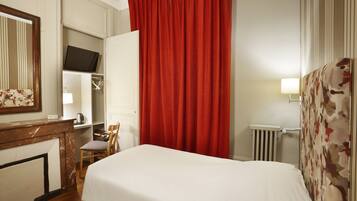 A hotel room with a bed, a chair, a desk with a mirror, a television, and a red curtain.
