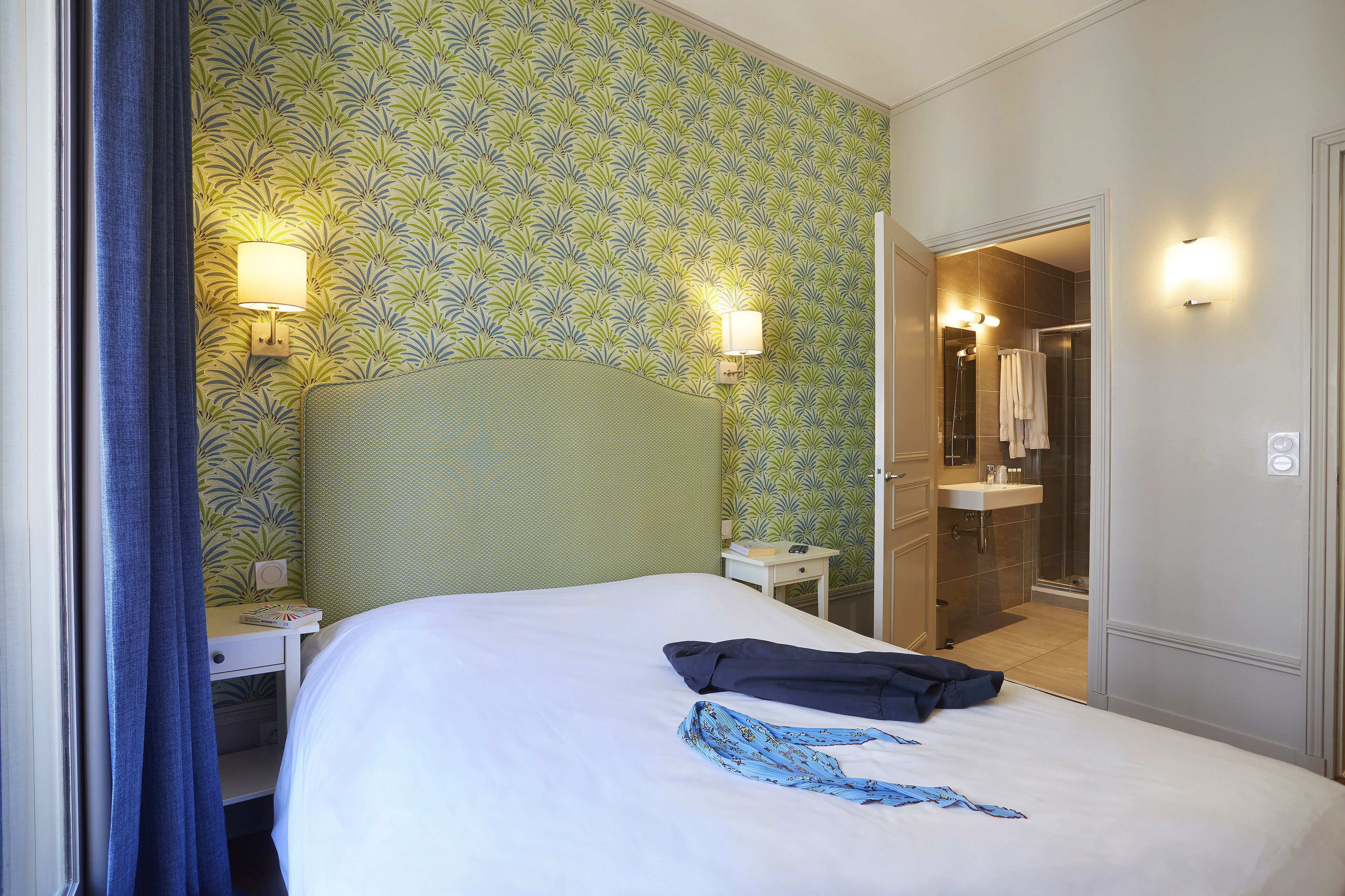 A hotel room with a bed, a nightstand, a lamp, and a bathroom visible through an open door.