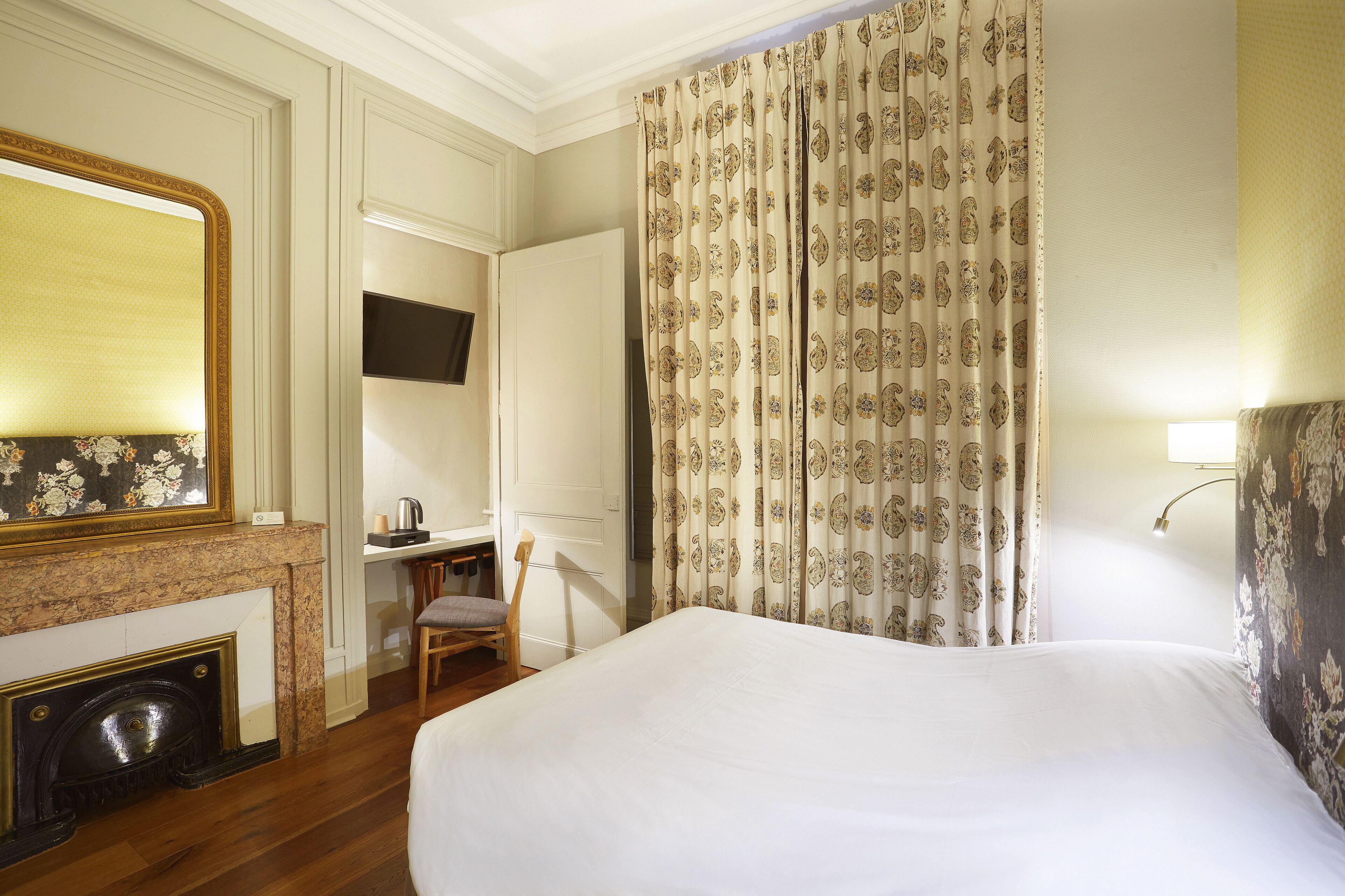 Une chambre d’hôtel avec un grand lit, une cheminée, un bureau avec une chaise et un téléviseur fixé au mur.