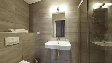 Un baño moderno con lavamanos blanco, cabina de ducha de vidrio y espejo integrado.