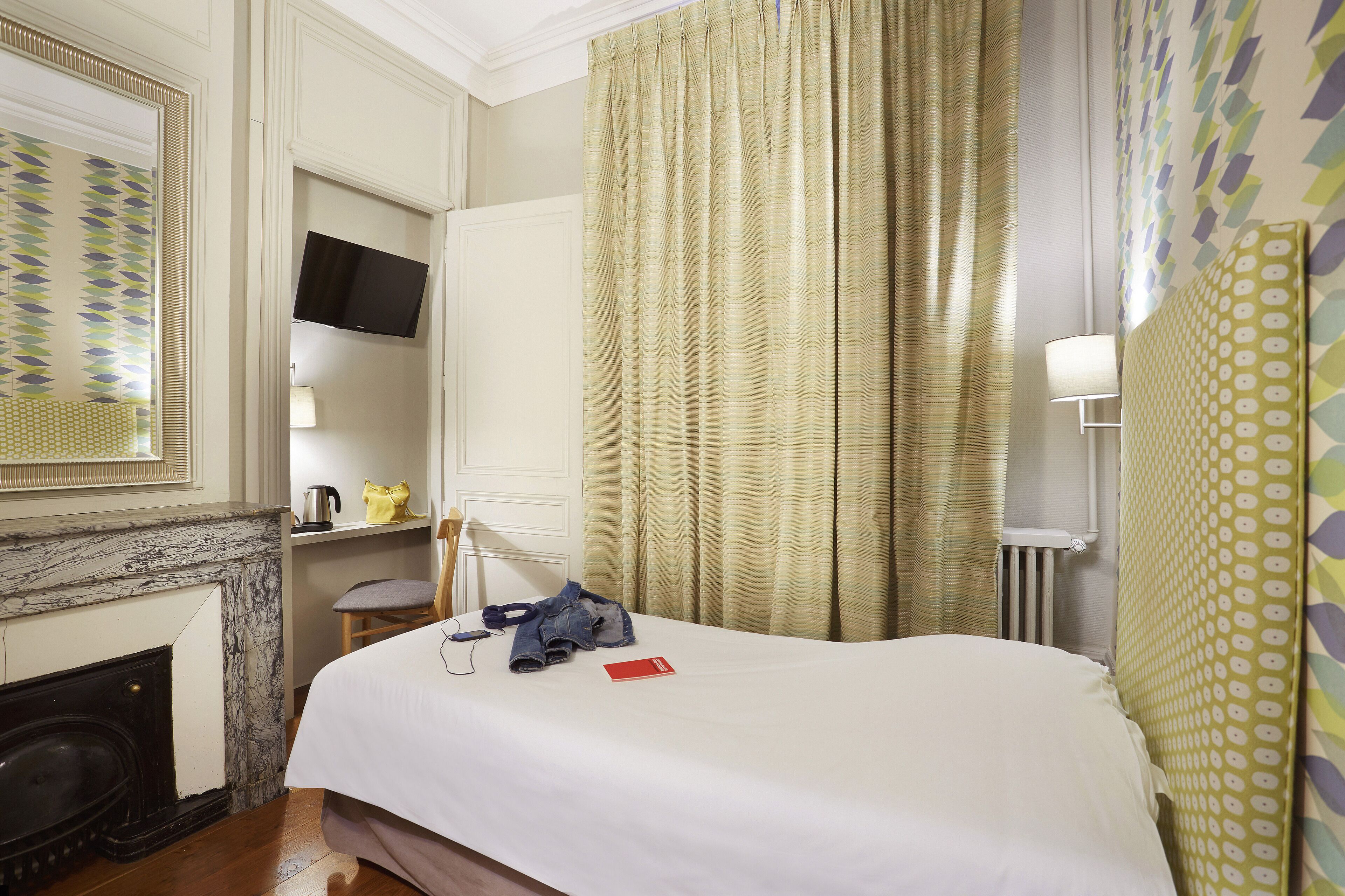 Una camera d'albergo con un letto, una televisione a parete, un camino e una finestra con tende.