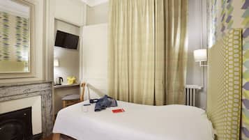 Una camera d'albergo con un letto, una televisione a parete, un camino e una finestra con tende.