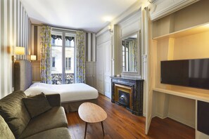 A hotel room with a bed, a sofa, a small table, a fireplace, and a TV. - Hotel Vaubecour (Lyon)