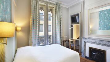 A hotel room with a bed, a desk, a chair, a fireplace, and a balcony with curtains.