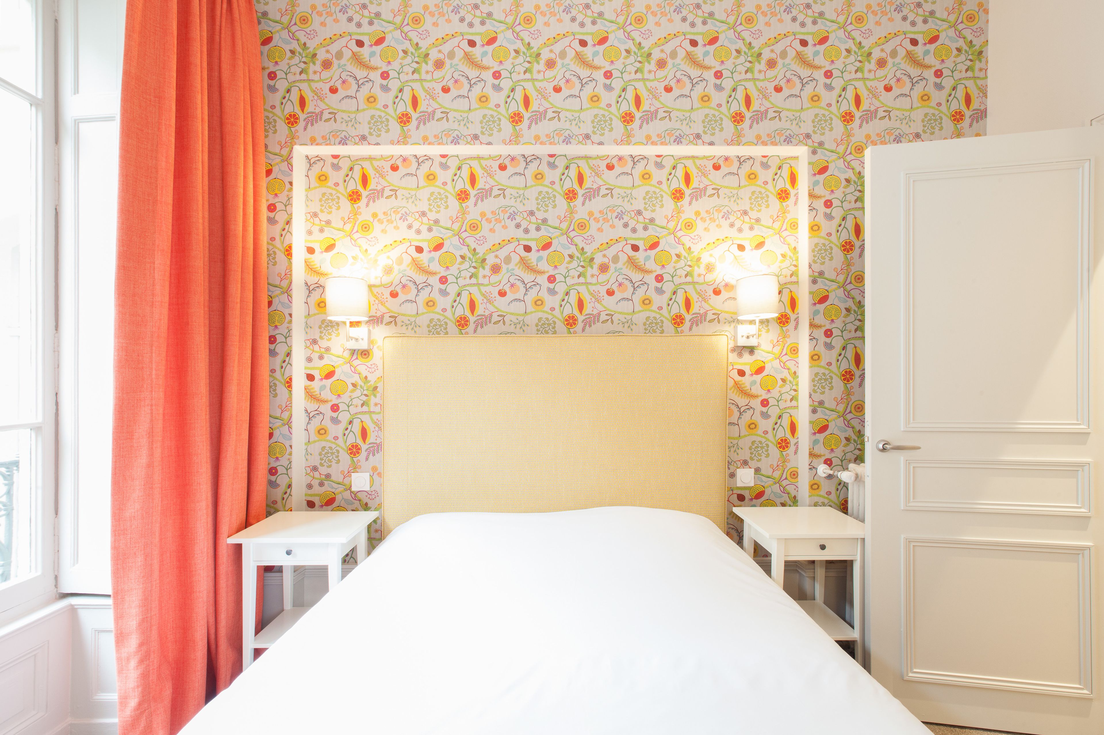 A neatly arranged bedroom with a bed, two bedside tables, a nightstand, a window with curtains, and a door.