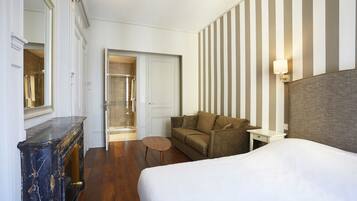 A hotel room with a bed, a sofa, a small table, a mirror, and a striped wall.