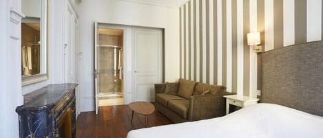 A hotel room with a bed, a sofa, a small table, a mirror, and a striped wall.