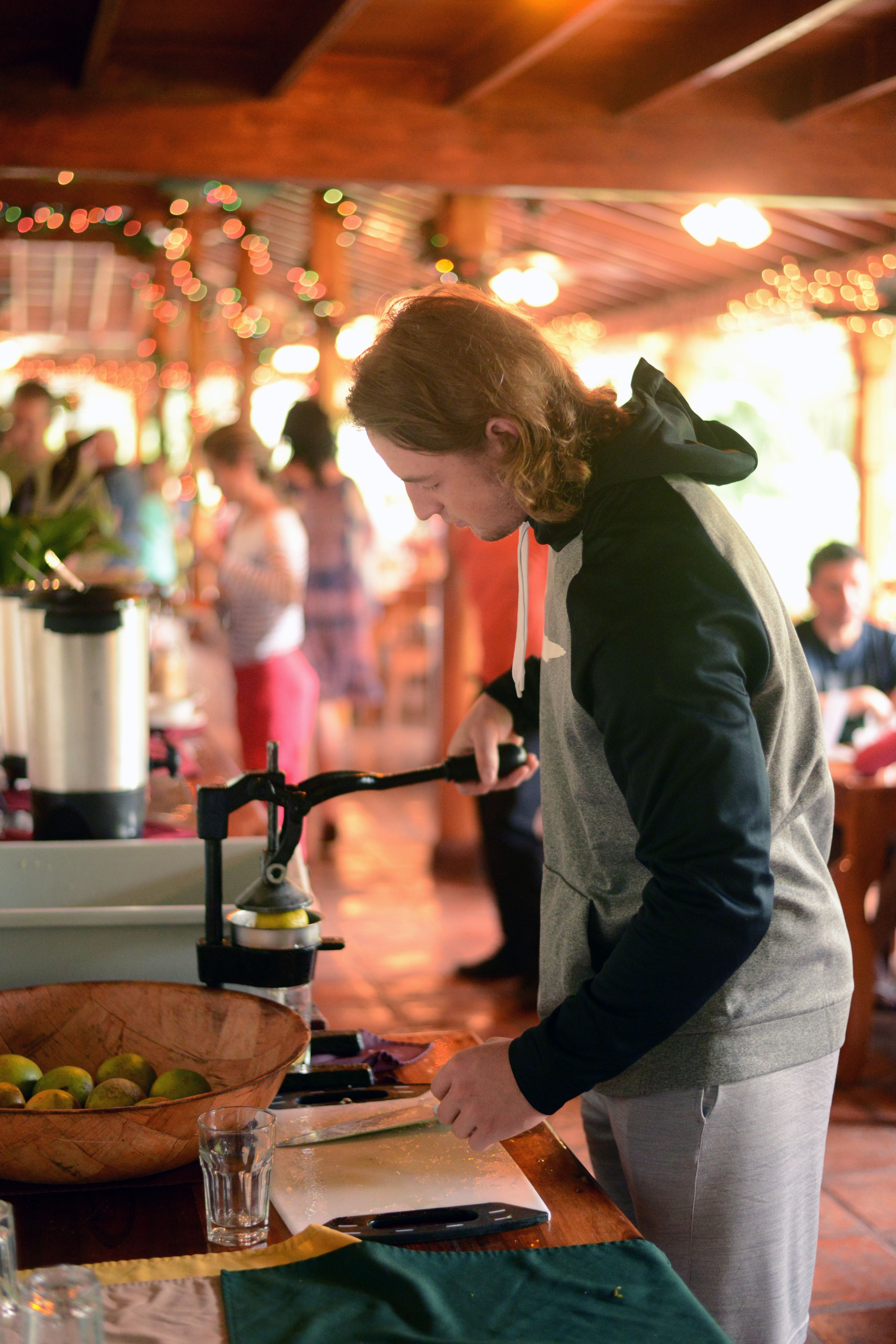 Une personne utilise un moulin à café manuel sur une table, à côté d’un bol de fruits et d’un verre d’eau.