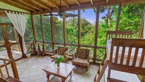 Habitación con piso de madera, ventanas amplias, muebles de madera y vista a vegetación exuberante.
