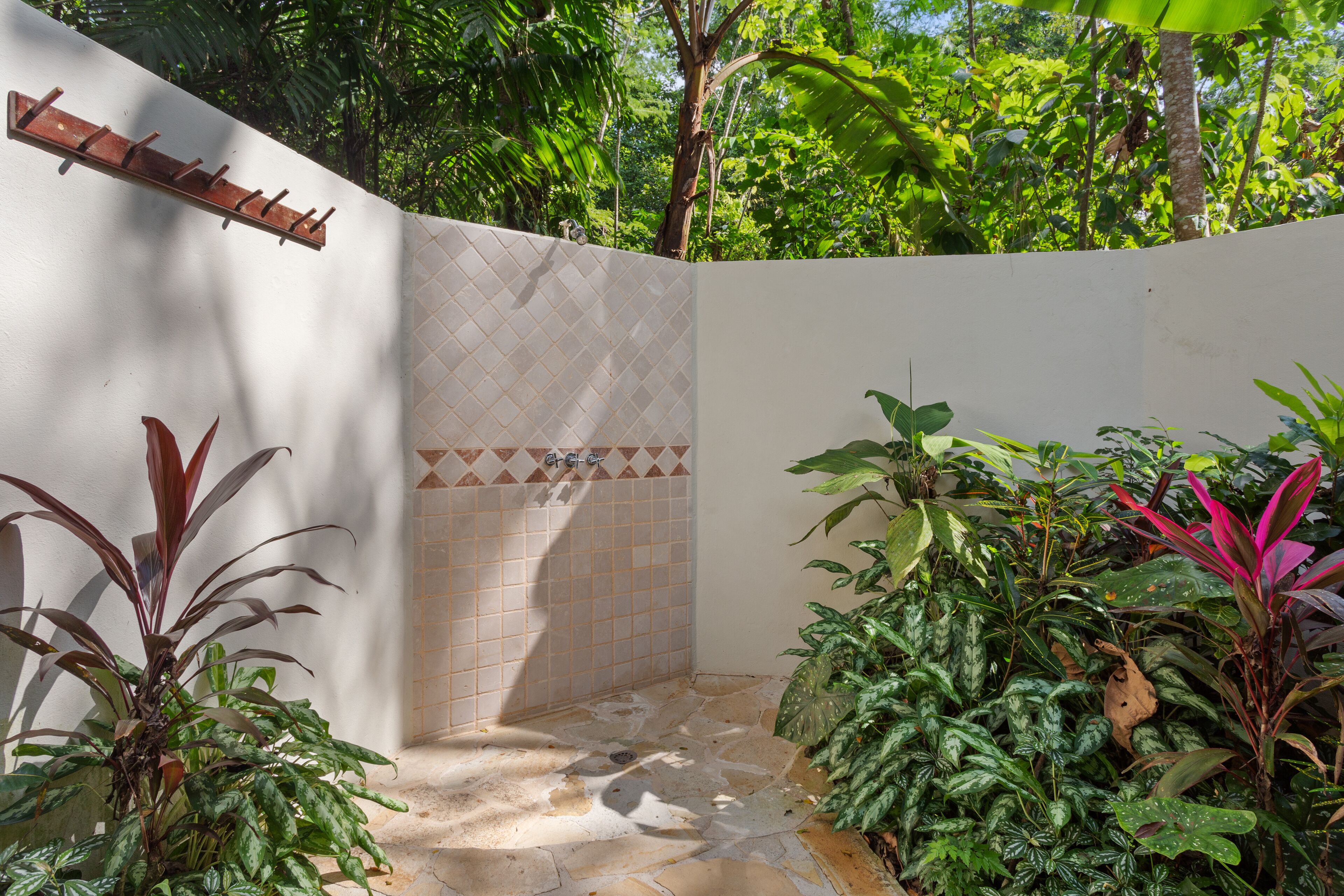 Un espace de douche carrelé, agrémenté d’une étagère en bois, le tout entouré d’une végétation luxuriante.