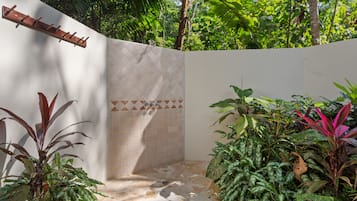 Un espace de douche carrelé, agrémenté d’une étagère en bois, le tout entouré d’une végétation luxuriante.