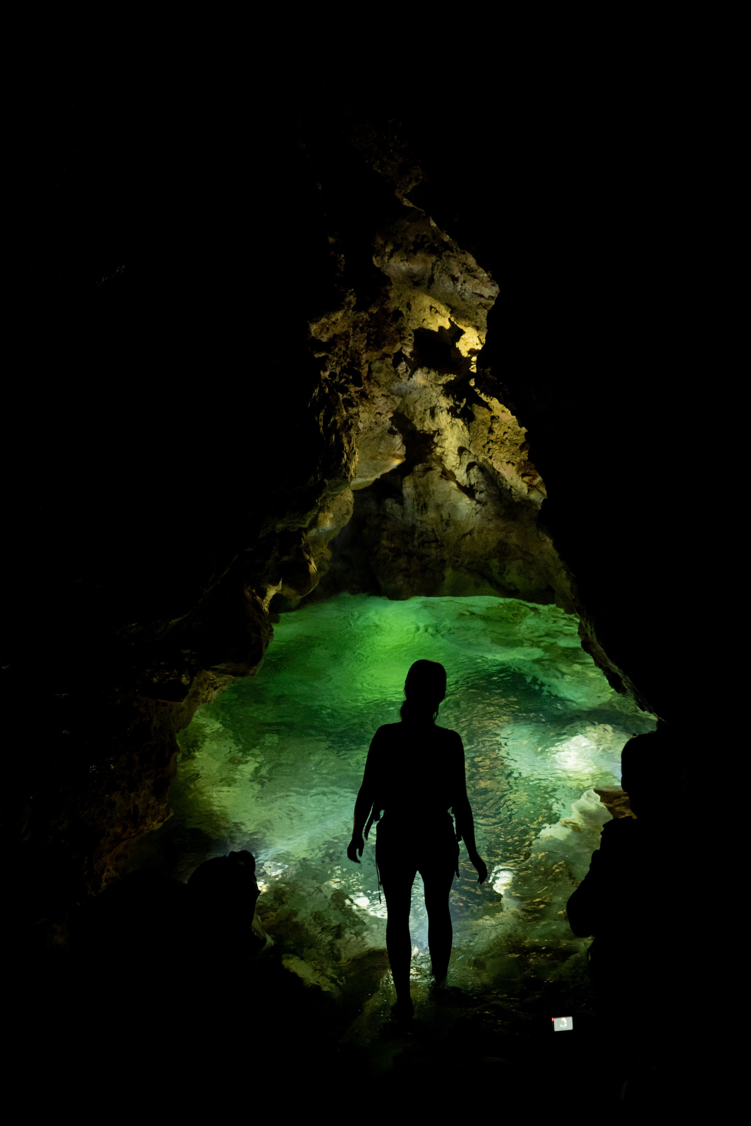Una persona de pie en una cueva con agua verdosa y paredes rocosas.