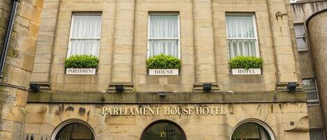 A historic building with a sign reading "Parliament House Hotel." It features a classic architectural style with large windows and a stone facade.