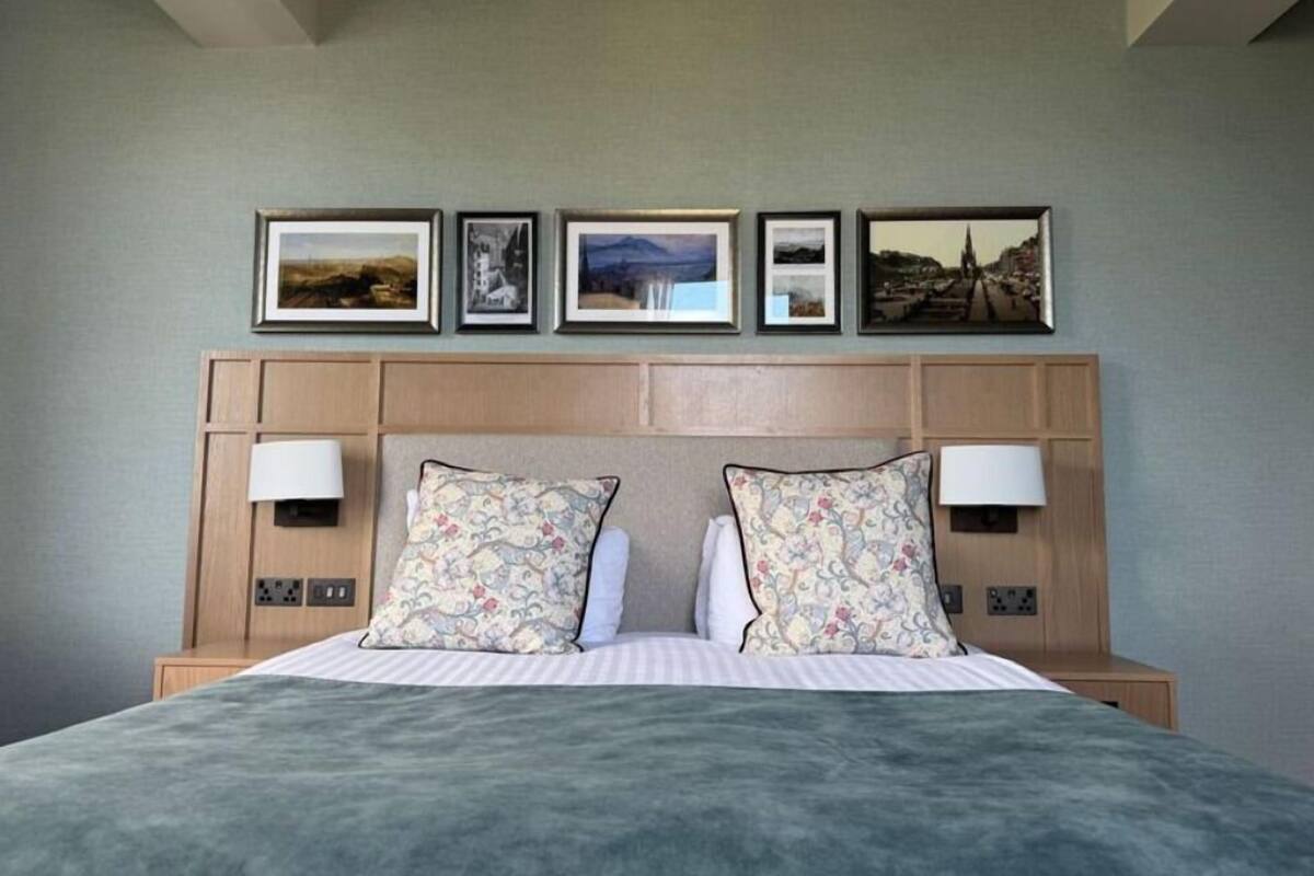 Une chambre d’hôtel avec un lit, deux lampes de chevet, une tête de lit ornée de tableaux encadrés et un mur aux couleurs neutres.