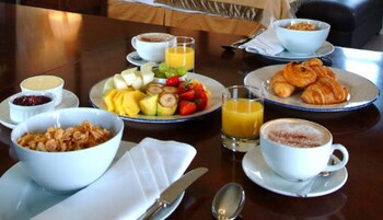 Une table de petit-déjeuner avec des assiettes de fruits, des croissants et du café.