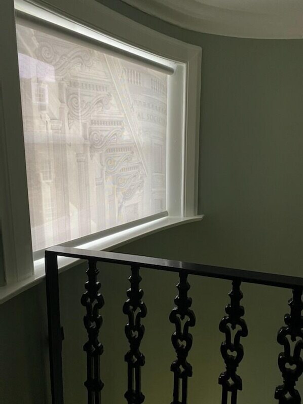 Una ventana con vista a la fachada de un edificio, un barandal negro y un muro verde.