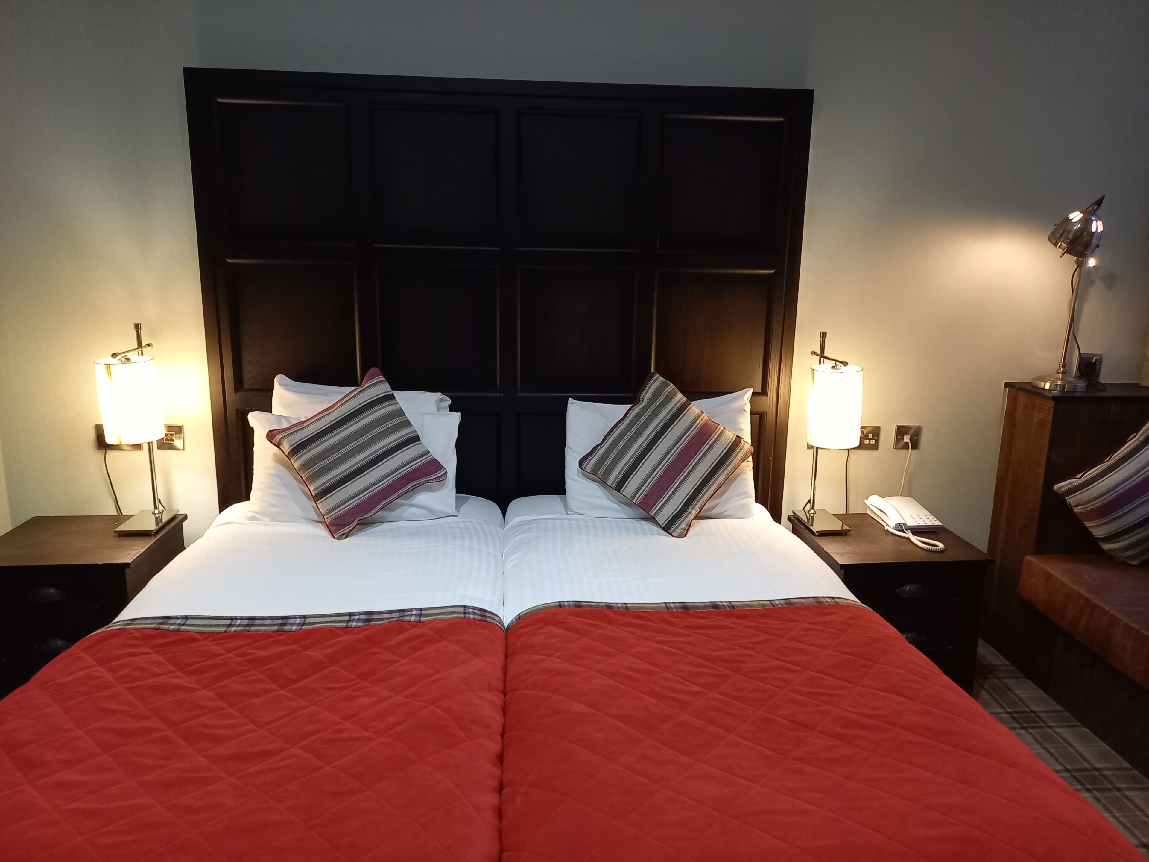 Un lit double avec une couette rouge, deux tables de chevet avec des lampes, un téléphone et une tête de lit sombre.