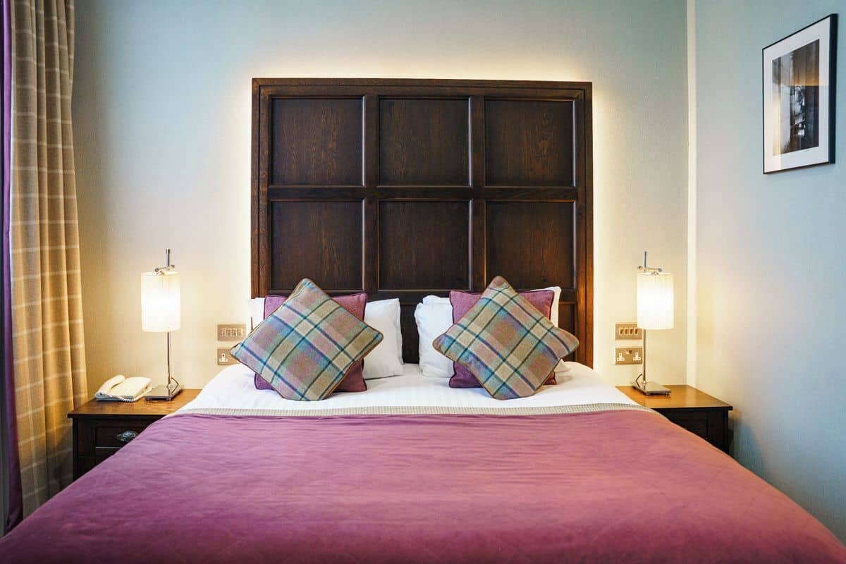 Une chambre d’hôtel avec un grand lit, deux tables de chevet, une commode, un téléphone et un tableau encadré au mur.